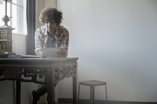 Loft living, A man sitting at a table by a window using a digital tablet, 