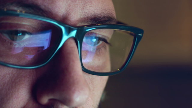 Portrait of a young man with glasses who works at night. Close up shot, display reflections