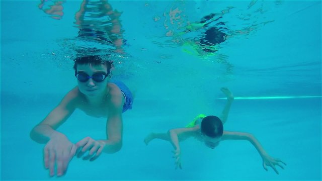 Teen boys swimming underwater in pool.
