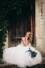 Beautiful young blond bride with bridal bouquet sitting on the stairs background gorgeous plants