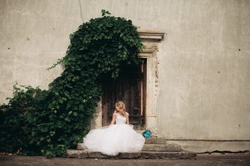 Beautiful young blond bride with bridal bouquet sitting on the stairs background gorgeous plants © olegparylyak