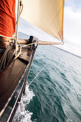 bow of a ship with a beige cotton jib sail filled by the wind with wooden mast, bowsprit and hull of an old rigging sailing boat during a sunny sea trip in brittany with a blur background - obrazy, fototapety, plakaty
