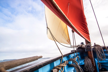 beige cotton jib sail and an ocher sail filled by the wind with wooden mast, bowsprit and hull of an old rigging sailing boat during a sunny sea trip in brittany