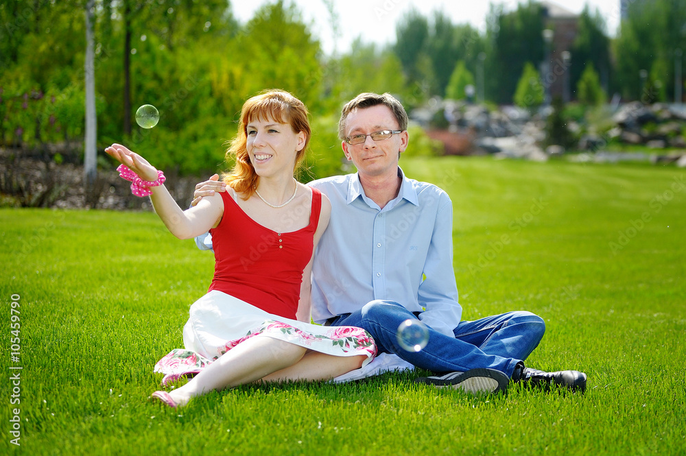 Wall mural couple love sitting on green grass in summer meadow