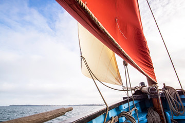beige cotton jib sail and an ocher sail filled by the wind with wooden mast, bowsprit and hull of...