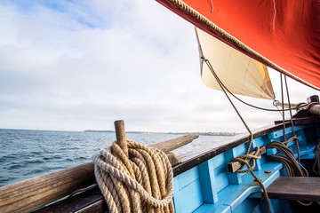 rope wound on a wooden cleat fixed on the hull of a rigging vintage sailing boat with a beige jib...