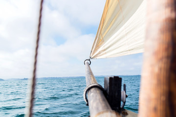 beige jib sail at the bow of a vintage sailing boat blew up by the wind with his wooden mast and...