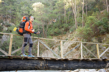 Fototapeta premium The man in the march with a backpack passes through the mountain river.