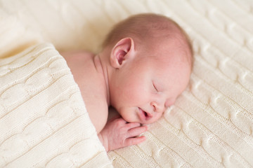 Tiny newborn baby sleeping on a soft knitted blanket