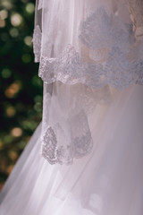 Gorgeous brunet bride in elegant dress holding bouquet and posing in the sunny summer park or garden on their wedding day. Portrait