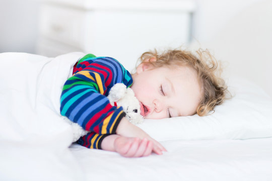 Adorable toddler girl taking a nap in a white bed