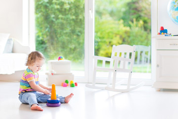 Cute toddler girl playing with a pyramid toy in a white room wit