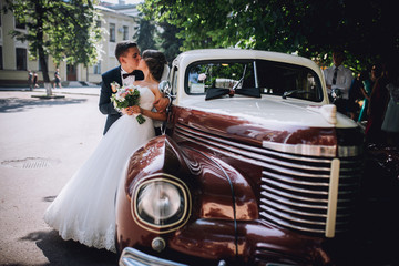 Happy bride and groom hugging and posing near old retro car