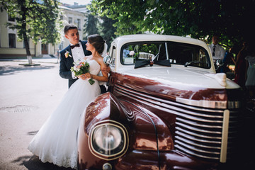 Happy bride and groom hugging and posing near old retro car