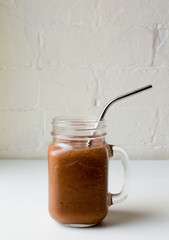 Berry smoothie in glass mug with metal straw on white table against white brick wall