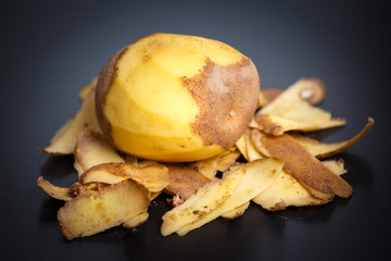 Raw peeled potatoes and potato peelings on black background