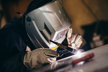 Manual worker doing his hard job using welding mask, tools and machinery on metal. Selective focus...