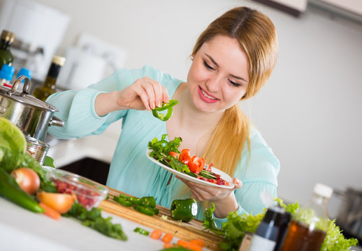 Young Woman Decorating Salad With Herbs In Kitchen