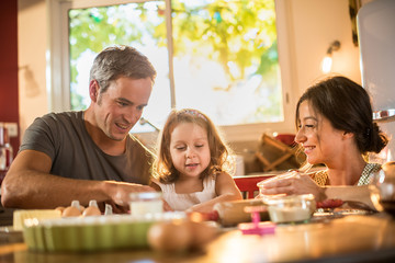 A four years old blonde girl is cooking cakes with parents
