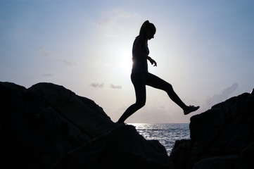 the young beautiful girl the sportswoman, in sportswear sneakers jumps through rocks at sunset, a...