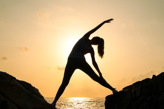 The woman practices yoga at dawn, there is an asana on a stone, dawn and an image of the girl, to enjoy dawn, to be happy with life, a beautiful body, ideal yoga,The girl meditates
