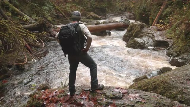 Backpacking Hiker Man Taking Cell Phone Picture at Scenic View of Raging River in Pacific Northwest Mountain Forest