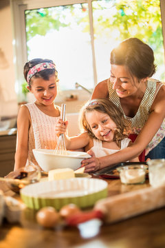 A mother is cooking a cake with her two young daughters
