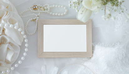 Blank wooden frame with flowers, jewelry, fur and accessories on white cloth background