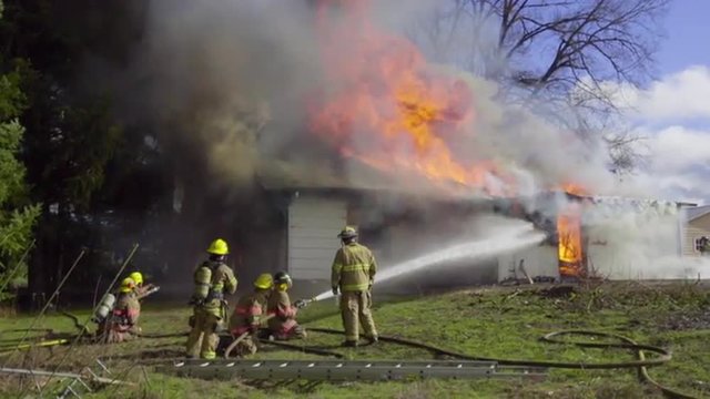 Wide shot of two hoses spraying water on a burning house 