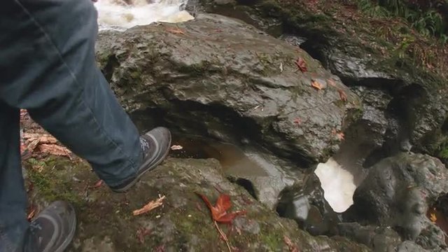 POV Low Angle of Hiker Boots Walking Along Riverbed Looking at Raging Canyon River Waterfall in Pacific Northwest Mountain Forest