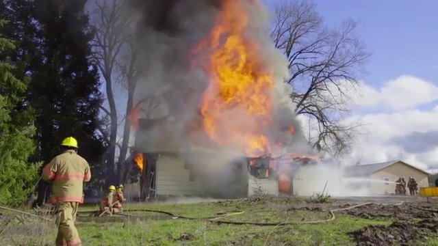 Firefighters spray water on huge flames from the front of a burning house
