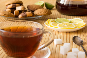 Black tea, cookies, sugar, lemon and lime on a table