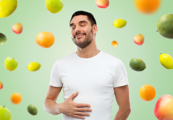happy full man touching tummy over falling fruits © Syda Productions