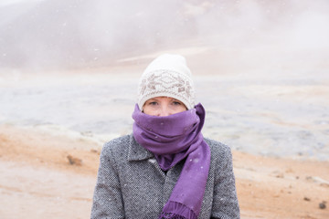 Woman with beanie and scarf standing in snow storm in Iceland with hot springs behind