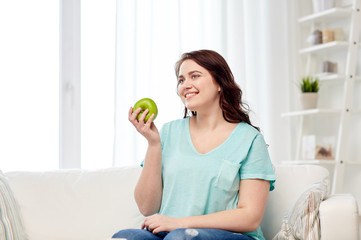 happy plus size woman eating green apple at home