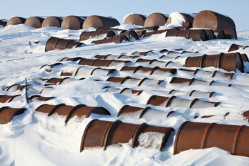 Arctic coast pollution. Rusting discarded oil barrels, oil drums in the arctic snow near abandoned...
