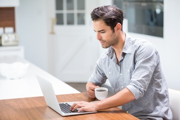 Fototapeta premium Young man holding coffee cup while working on laptop