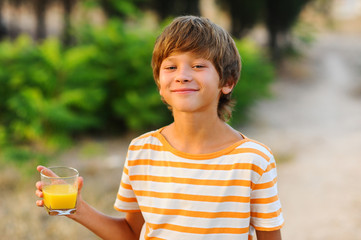 Smiling young boy holding glass with orange juice outdoors at green background