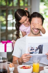Happy daughter covering father eyes while holding gift box 