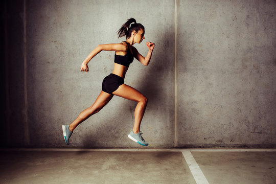 Slim attractive sportswoman running against a concrete wall