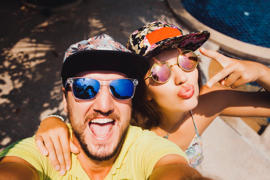 beautiful couple in caps and sunglasses make the selfi to the camera compared to the pool
