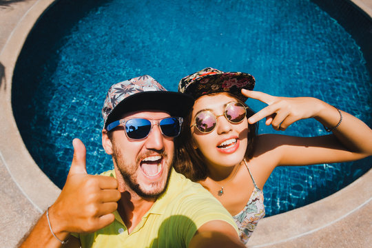beautiful couple in caps and sunglasses make the selfi to the camera compared to the pool