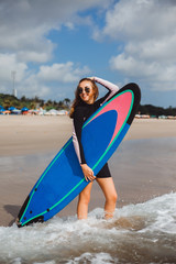 young girl in a black wetsuit with surfboard awaits brought waves for surfing, surfing at sunset, catch the wave, ride the wave sports fitness, sandy beach ocean bali indonesia