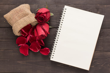 Red roses flowers and a notebook are on the wooden background