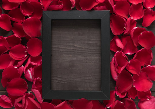 Beautiful red rose petals and frame picture are on the wooden ba