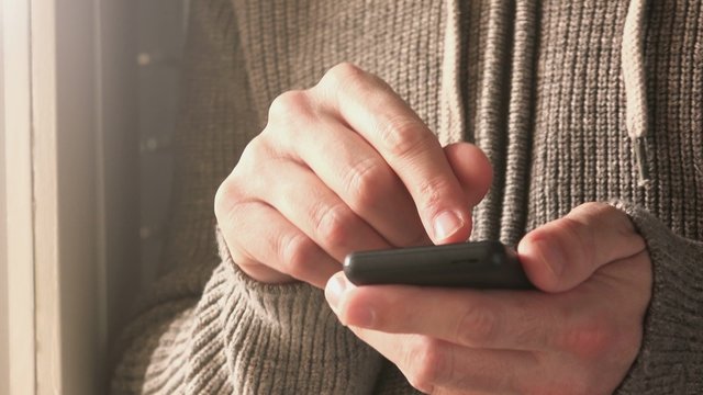Man using mobile smartphone for texting messages, adult male person standing by the window of dark living room sending SMS with smart phone app, selective focus with shallow depth of field.