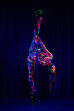 Female pole dancer in bright neon colours under ultraviolet (UV) light on background