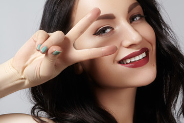 Closeup studio portrait of beautiful sexy young woman with gesturing peace. Perfect retro style ang fashion make-up. happy toothy smile with red lips makeup