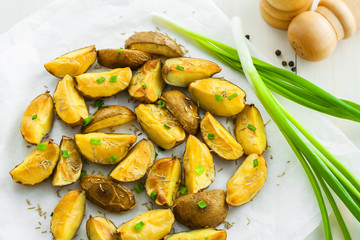 Fresh baked potato wedges with rosemary and spring onion on table, top view
