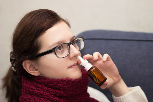 Sick woman in a scarf with spray for the nose